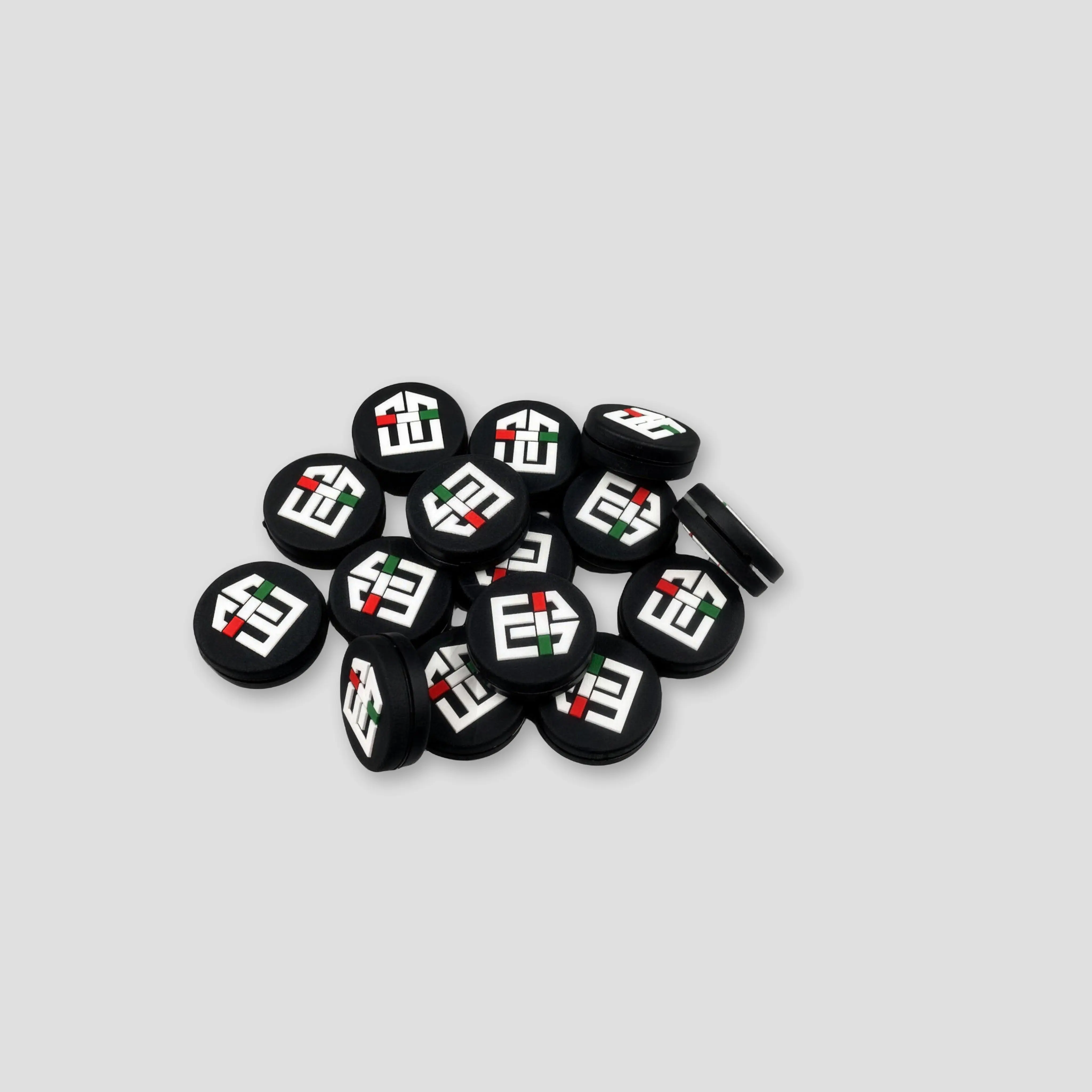 A finished pile of black custom tennis dampeners with raised white, red, and green logo details