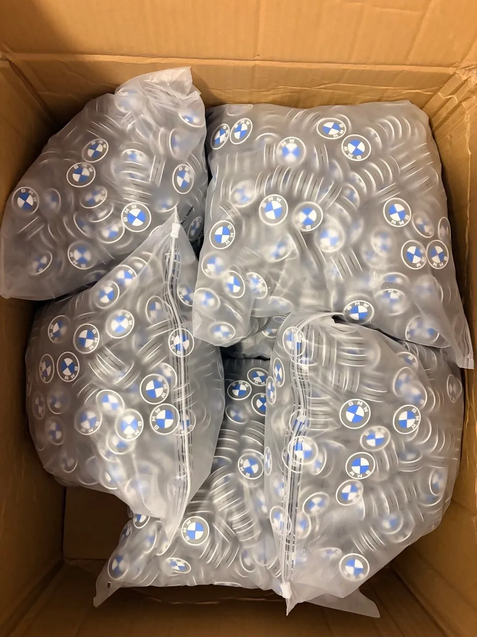 A completed client order of BMW-logo tennis dampeners packed in sealed bags inside a shipping carton