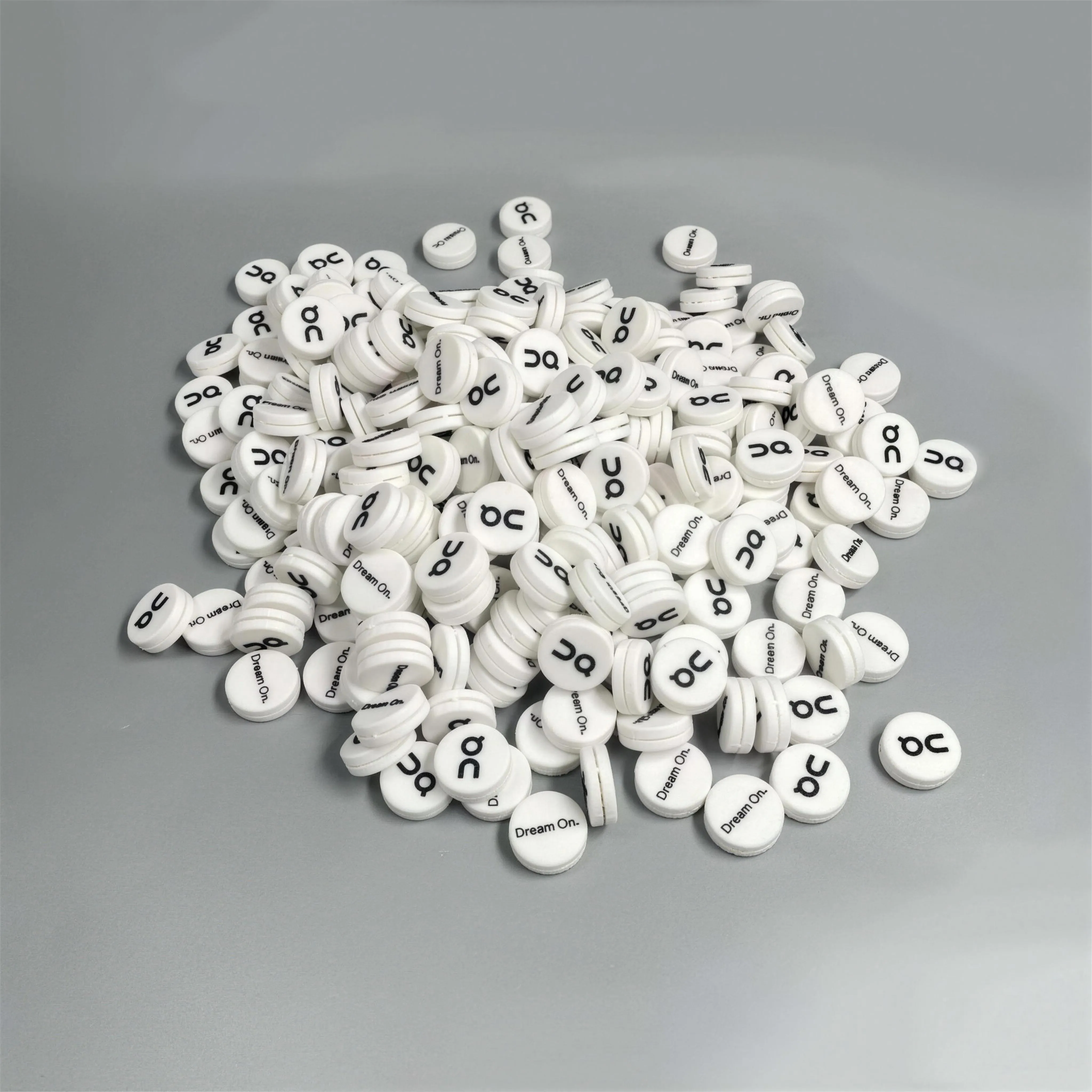 A large production order of white On Running custom tennis dampeners on a gray surface